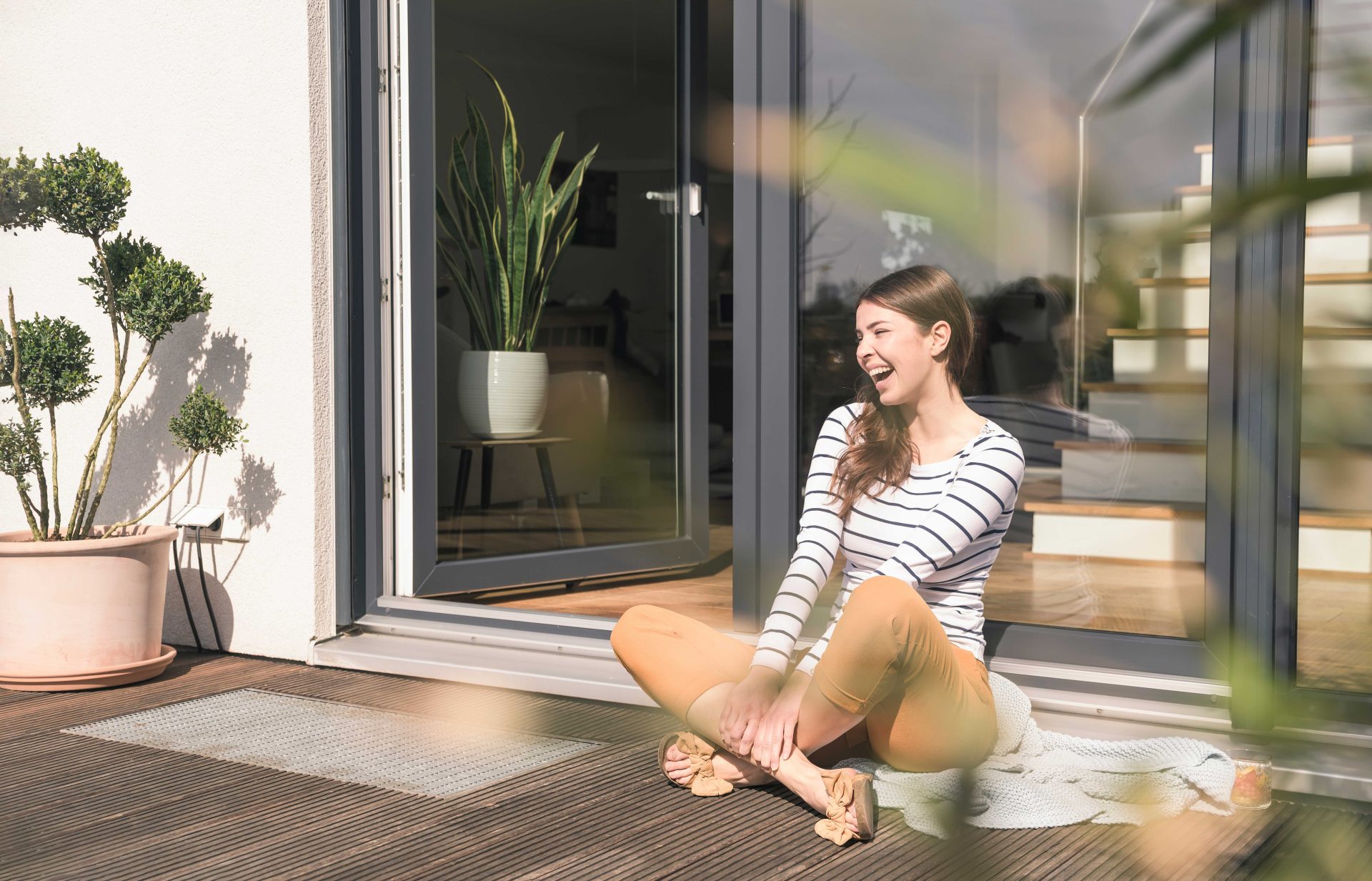 Jeune femme assise en tailleur et heureuse sur sa terrasse en bois.