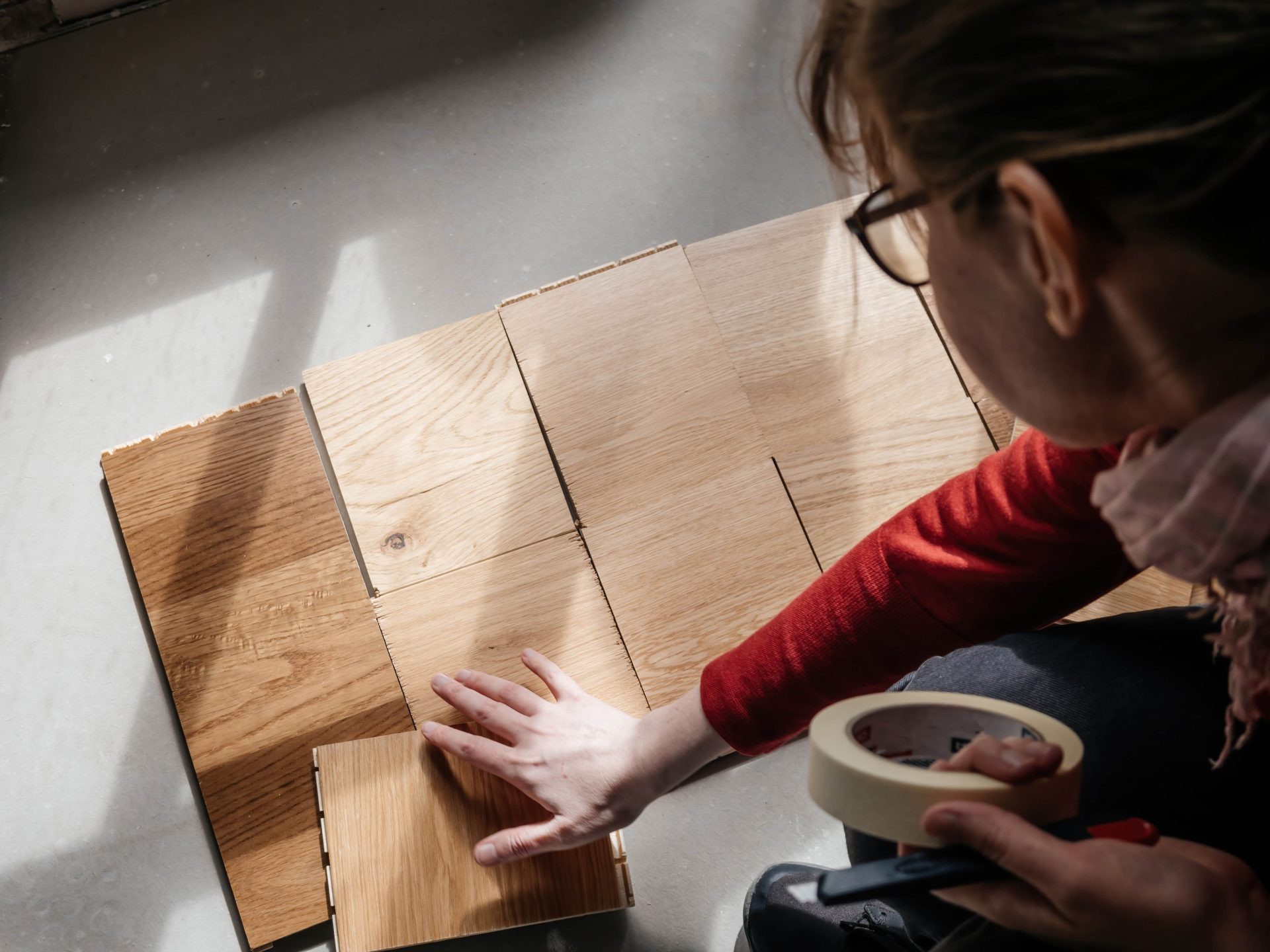 Vue de dessus d'une femme brune avec des lunettes choisissant plusieurs parquets en bois de différents fabricants et différentes nuances dans sa nouvelle maison. 