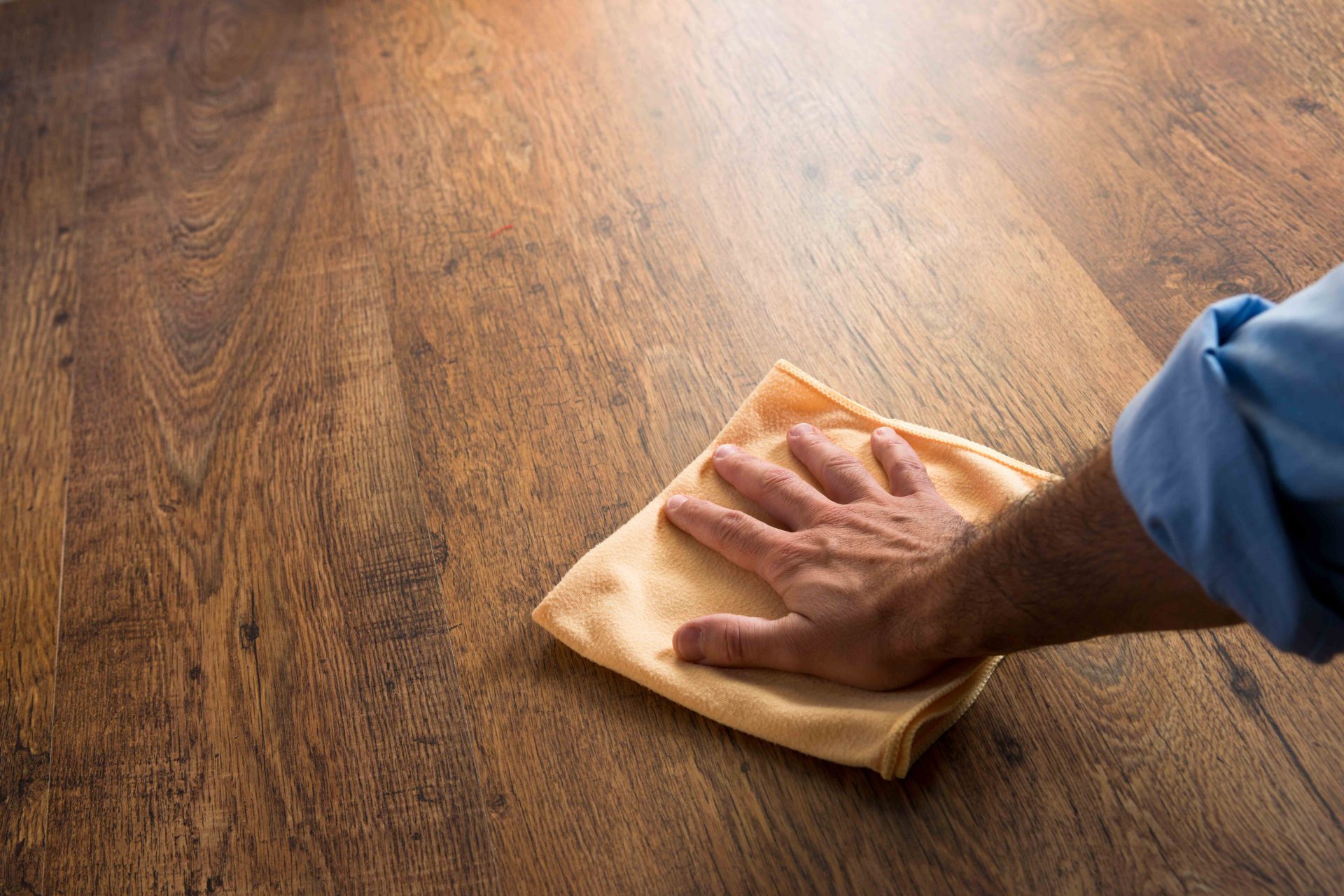 Main en train de nettoyer et entretenir un sol en parquet en bois foncé